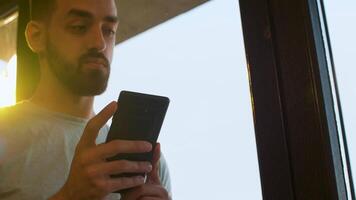 sélectif concentrer sur directeur téléphone près une gros fenêtre dans chaud le coucher du soleil lumière. lent mouvement coup video