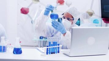 Female scientist looking at reactive blue solution and writing formula. Smoking blue solution in test tubes. video