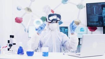 fêmea cientista com virtual realidade fone de ouvido dentro moderno química laboratório. cientista segurando teste tubos com azul solução dentro a fundo. video