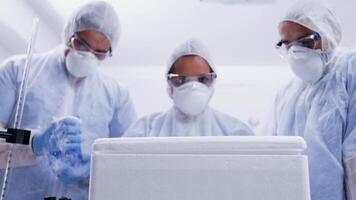 Team of scientist looking closely in a refrigerator box and taking out a smoking virus in contact with air. Scientist in coverall protection equipment. video