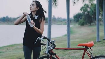 Lycklig ung asiatisk kvinna medan ridning en cykel i en stad parkera. hon log använder sig av de cykel av transport. miljömässigt vänlig begrepp. video
