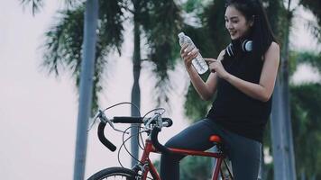 contento joven asiático mujer mientras montando un bicicleta en un ciudad parque. ella sonrió utilizando el bicicleta de transporte. ambientalmente simpático concepto. video