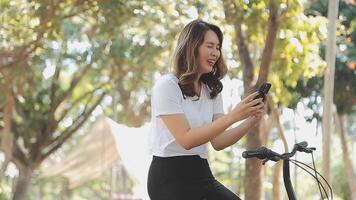 contento asiático hermosa joven mujer montando bicicleta en calle al aire libre cerca edificio ciudad, retrato de sonriente hembra estilo de vida utilizando bicicleta en verano viaje medio de transporte, eco simpático video