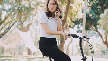 contento asiático hermosa joven mujer montando bicicleta en calle al aire libre cerca edificio ciudad, retrato de sonriente hembra estilo de vida utilizando bicicleta en verano viaje medio de transporte, eco simpático video