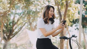 contento asiático hermosa joven mujer montando bicicleta en calle al aire libre cerca edificio ciudad, retrato de sonriente hembra estilo de vida utilizando bicicleta en verano viaje medio de transporte, eco simpático video