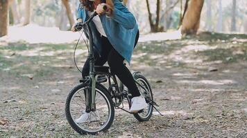 contento asiático hermosa joven mujer montando bicicleta en calle al aire libre cerca edificio ciudad, retrato de sonriente hembra estilo de vida utilizando bicicleta en verano viaje medio de transporte, eco simpático video