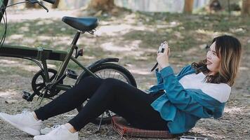 contento asiatico bellissimo giovane donna equitazione bicicletta su strada all'aperto vicino edificio città, ritratto di sorridente femmina stile di vita utilizzando bicicletta nel estate viaggio si intende di trasporto, eco amichevole video