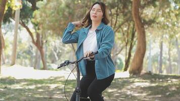 contento asiático hermosa joven mujer montando bicicleta en calle al aire libre cerca edificio ciudad, retrato de sonriente hembra estilo de vida utilizando bicicleta en verano viaje medio de transporte, eco simpático video
