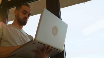 Low angle shot of manager working on the laptop near a window. Warm sunset light from behind. Handheld slow motion shot video