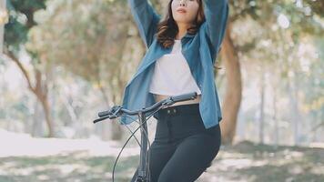 contento asiático hermosa joven mujer montando bicicleta en calle al aire libre cerca edificio ciudad, retrato de sonriente hembra estilo de vida utilizando bicicleta en verano viaje medio de transporte, eco simpático video