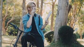 retrato do uma feliz jovem homem vestido dentro camisa com saco equitação em uma bicicleta ao ar livre video