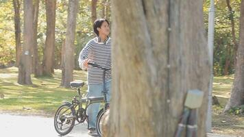 gezond en actief levensstijl, gaan naar werk Aan eco vervoer. glimlachen aantrekkelijk millennial mannetje werknemer in bril met zak en kop van meenemen koffie, in beweging fiets in stad park in zomer, buitenshuis video