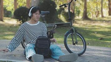 Healthy and active lifestyle, going to work on eco transport. Smiling attractive millennial male employee in glasses with bag and cup of takeaway coffee, moving bike in city park in summer, outdoor video