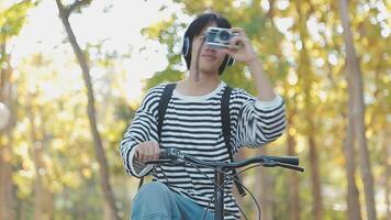 sano y activo estilo de vida, yendo a trabajo en eco transporte. sonriente atractivo milenario masculino empleado en lentes con bolso y taza de para llevar café, Moviente bicicleta en ciudad parque en verano, al aire libre video