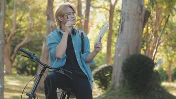 retrato do uma feliz jovem homem vestido dentro camisa com saco equitação em uma bicicleta ao ar livre video