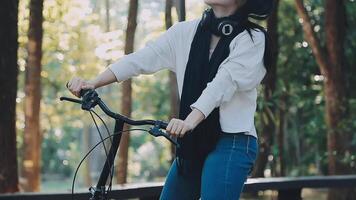 content femme dans jeans vêtements supporter près vélo bicyclette sur trottoir dans vert parc en plein air utilisation mobile cellule téléphone 13 pro bavarder en ligne. gens actif Urbain en bonne santé mode de vie cyclisme concept video
