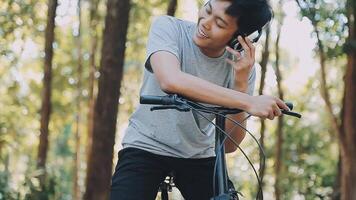 un hermoso joven hombre va a el ciudad con su bicicleta. él es sentado en un bicicleta y enviando texto mensaje en el teléfono inteligente video