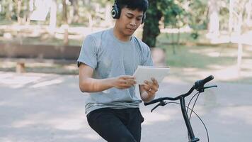 un hermoso joven hombre va a el ciudad con su bicicleta. él es sentado en un bicicleta y enviando texto mensaje en el teléfono inteligente video