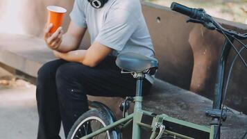 un hermoso joven hombre va a el ciudad con su bicicleta. él es sentado en un bicicleta y enviando texto mensaje en el teléfono inteligente video