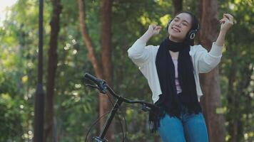 contento mujer en pantalones ropa estar cerca bicicleta bicicleta en acera en verde parque al aire libre utilizar móvil célula teléfono 13 Pro charla en línea. personas activo urbano sano estilo de vida ciclismo concepto video