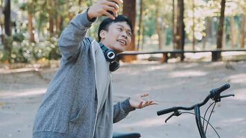 A handsome young man goes to the city with his bike. He is sitting on a bike and sending text message on the smartphone. video