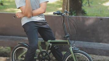 un hermoso joven hombre va a el ciudad con su bicicleta. él es sentado en un bicicleta y enviando texto mensaje en el teléfono inteligente video