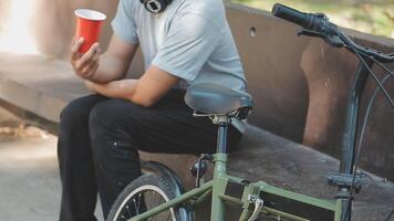 ein gut aussehend jung Mann geht zu das Stadt mit seine Fahrrad. er ist Sitzung auf ein Fahrrad und Senden Text Botschaft auf das Smartphone. video