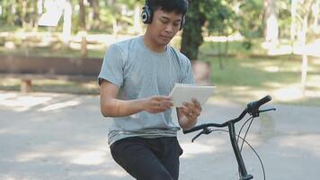 une Beau Jeune homme va à le ville avec le sien vélo. il est séance sur une bicyclette et Envoi en cours texte message sur le téléphone intelligent. video