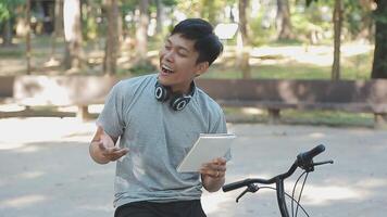 un hermoso joven hombre va a el ciudad con su bicicleta. él es sentado en un bicicleta y enviando texto mensaje en el teléfono inteligente video