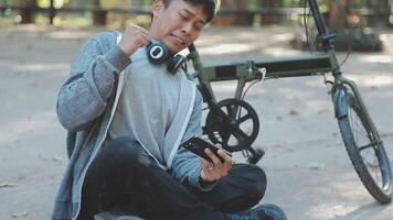 A handsome young man goes to the city with his bike. He is sitting on a bike and sending text message on the smartphone. video
