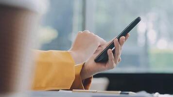 Woman hand holding white mobile phone on a table with a laptop in office. video