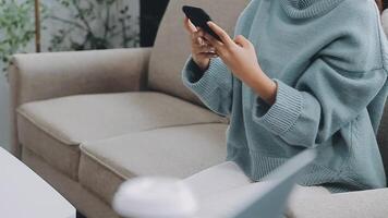 Woman hand holding white mobile phone on a table with a laptop in office. video