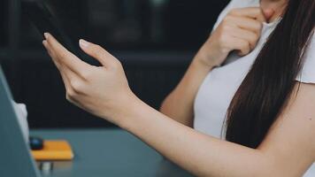vrouw hand- Holding wit mobiel telefoon Aan een tafel met een laptop in kantoor. video