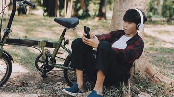 Asian man traveller using smart phone while sitting in the city park on beautiful day. Travel, vacation and journey concept video
