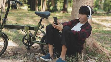 Asian man traveller using smart phone while sitting in the city park on beautiful day. Travel, vacation and journey concept video