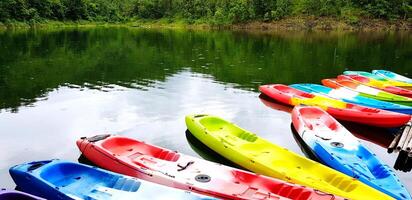 Many colorful canoeing or kayak boat parked on the rive for tourist and customers rent them with green tree plant background and copy space at Srinagarind Dam lake, Kanchanaburi Province, Thailand photo