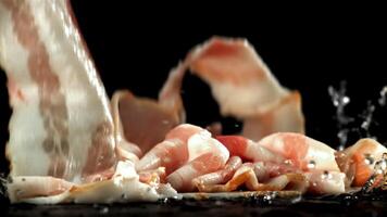 Fresh bacon falling on black background. Filmed on a high-speed camera at 1000 fps. High quality FullHD footage video