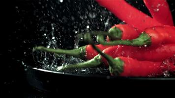 The chili peppers fall with splashes into the plate. On a black background. Filmed on a high-speed camera at 1000 fps. High quality FullHD footage video