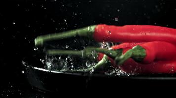 The chili peppers fall with splashes into the plate. On a black background. Filmed on a high-speed camera at 1000 fps. High quality FullHD footage video