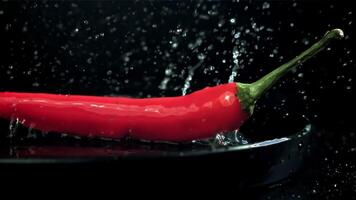 The chili peppers fall with splashes into the plate. On a black background. Filmed on a high-speed camera at 1000 fps. High quality FullHD footage video