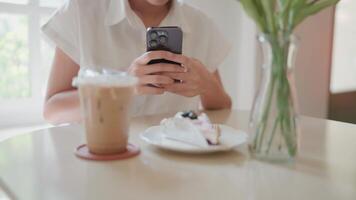 jung Mädchen sitzt und nimmt Fotos von Kuchen und Latté Kaffee Getränke im ein minimalistisch Geschäft mit Morgen Brisen und Sonnenschein. video