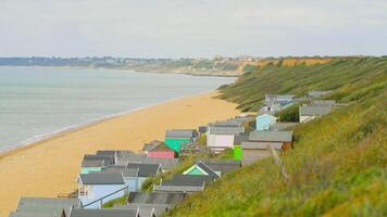 A line of bright vibrant colorful beach huts on the south coast of England. View from the top of a cliff looking down over the sheds and out to the sea video