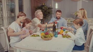 multigénérationnel famille Heureusement souriant et tintement des lunettes ensemble dans une pain grillé tandis que ayant vacances dîner fête à maison. video