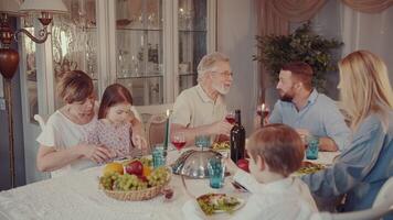 Happy young and senior family members smiling and clinking wine glasses together in a toast while having holiday dinner at home. video