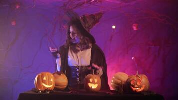A beautiful and funny witch is dancing near the burning pumpkins. Halloween celebration. video