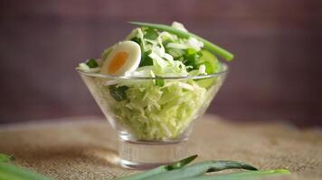 spring salad with early cabbage, cucumbers, eggs and green onions on a wooden table. video