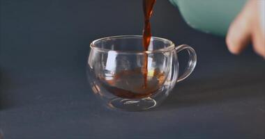 Black tea is poured from a thermos into a transparent cup. ANAMORPHOUS effect video