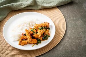 stir-fried fried fish with basil and chili in thai style topped on rice photo