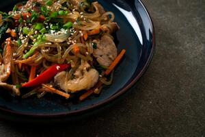 japchae or stir-fried Korean vermicelli noodles with vegetables and pork topped with white sesame photo