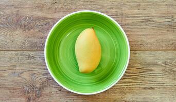 pale yellow mango on a green plate on a wooden tabletop photo